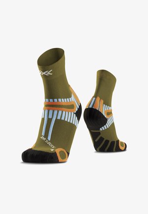 Paire de chaussettes de sport vert olive avec des motifs géométriques noirs, orange et bleus, présentées sur des formes en forme de pied sur fond blanc.