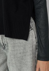 Czarny prążkowany sweter z bocznymi rozcięciami, w połączeniu z jasnoszarymi podniszczonymi dżinsami. Sweter ma gładką, dzianą fakturę i luźny fason.