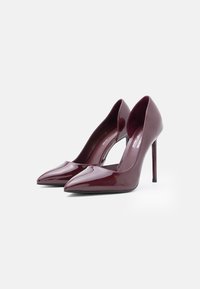 Burgundy patent leather high heels with pointed toes, sleek design, and stiletto heels. Smooth, shiny surface and open sides.