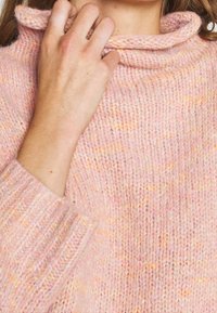 Ljust rosa stickad tröja med krage, som har ett texturerat mönster och ribbade muddarna. Mjuk material med subtila orange fläckar.