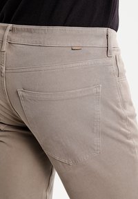 Beige denim broek met een gladde textuur, voorzien van een achterzak en subtiele stikseldetails, ontworpen voor een aansluitende silhouet.