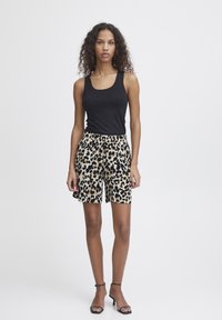 Crna majica bez rukava u kombinaciji s kratkim hlačama do koljena s bež podlogom i crno-smešastim leopard uzorkom. Model nosi crne sandale sa trakama.