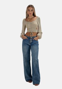 Blusa beige a croppata con maniche a sbuffo e dettaglio con cordoncino abbinata a jeans a vita alta svasati di colore blu chiaro. Tessuto morbido, vestibilità rilassata.
