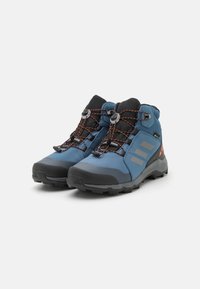 Botas de senderismo azules hechas de material sintético, con un upper texturizado, suela de goma y acentos negros. Presentan franjas reflectantes y un sistema de lazado rápido.