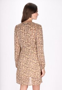 Bloemrijke jurk in lichtbeige met paarse en groene accenten; lange mouwen, gathered taille en licht doorschijnende stof.