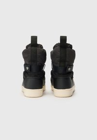 Zapatillas altas negras hechas de cuero y tela, con puños elásticos, correas de velcro y una suela de goma blanca.