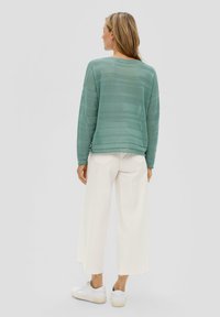 Lichtgroene, getextureerde gebreide trui met een losse pasvorm en brede mouwen, gecombineerd met witte wijde pantalons en witte sneakers.