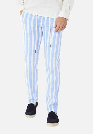 Uomo che indossa pantaloni a righe verticali azzurro chiaro e bianco con coulisse bianche e scarpe slip-on blu scuro.