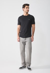 Black cotton t-shirt with a crew neck and short sleeves, paired with light gray jeans and black and white sneakers. Subtle embroidered logo.