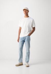 Lettet hvid t-shirt, lyseblå jeans og beige sneakers. En beige kasket fuldender outfittet. Simpelt design og afslappet pasform.