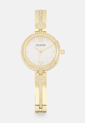 Gold bracelet watch with a round white face, crystal embellishments, and Roman numerals. Heart-shaped accents detail the band.