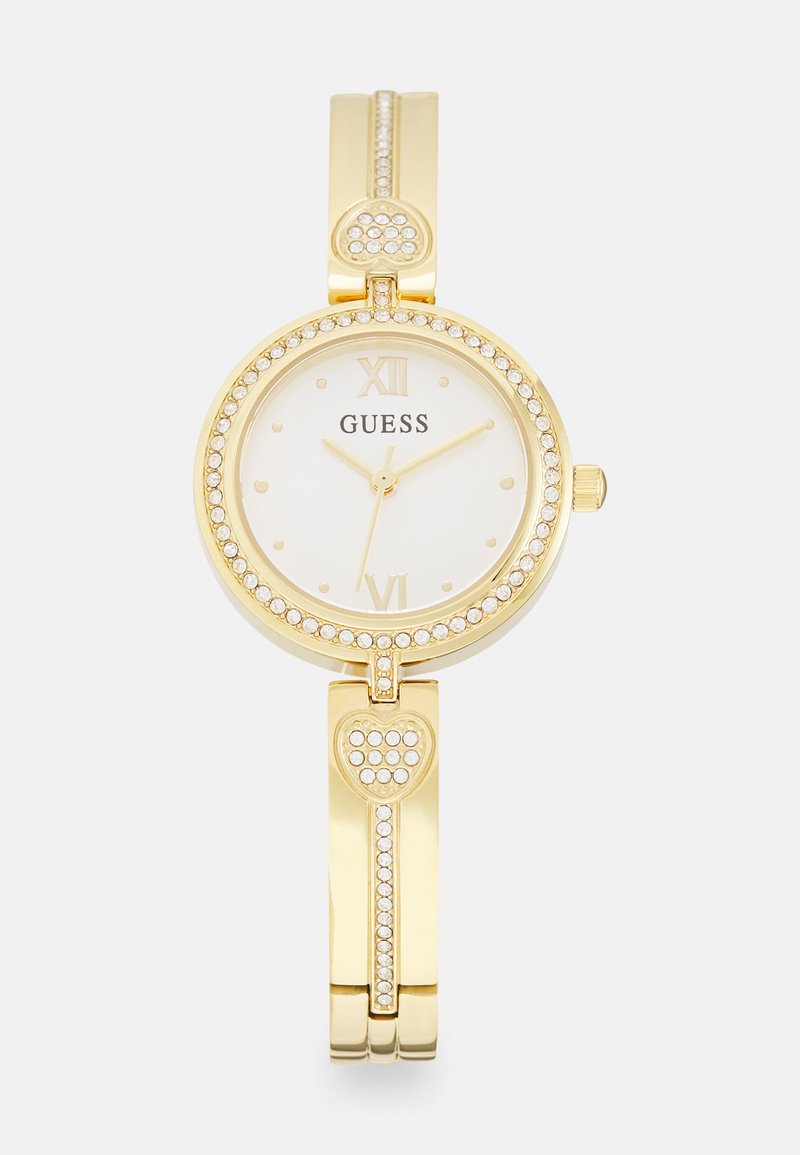 Relógio de pulso dourado com um mostrador redondo branco, detalhes em cristal e números romanos. A pulseira possui acentos em forma de coração.