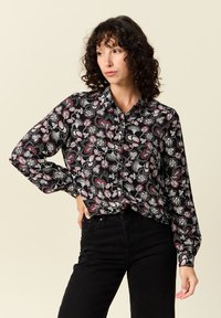 Svart skjorta med knappar och ett blommigt och paisleymönster i rött och vitt. Långa ärmar och klassisk krage. Bärs med svarta jeans.