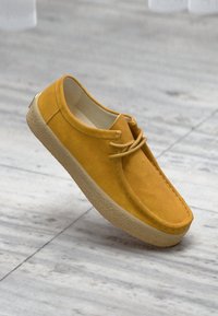 Gelbe Wildlederschuhe mit abgerundetem Zehenbereich, Schnürdesign und einer strukturierten Gummisohle. Glatte Innenauskleidung und minimale Nähdetails.