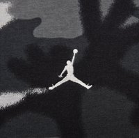 Camouflage-mønsteret stof i nuancer af grå har et hvidt broderet Jumpman-logo, der fremviser atletisk bevægelse og dynamisk design.