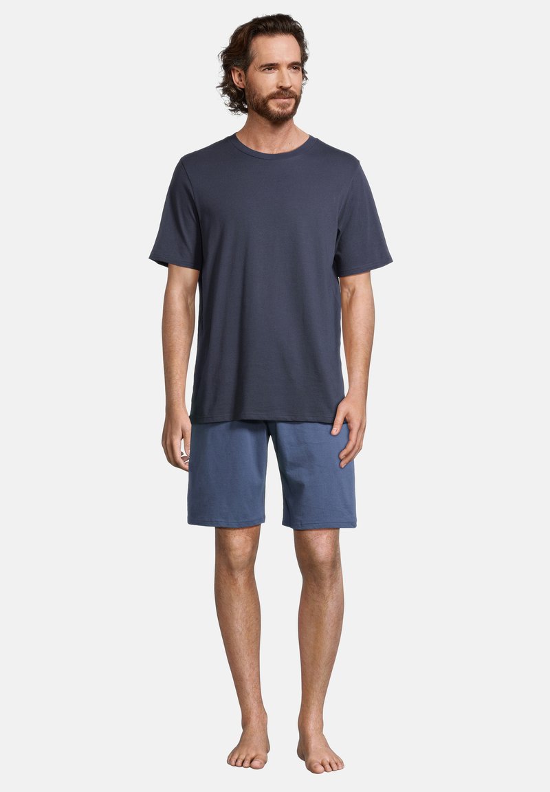 T-shirt in cotone blu navy con maniche corte, abbinata a pantaloni corti in cotone di colore azzurro chiaro. Vestibilità casual, senza fantasie o decorazioni, indossata a piedi nudi.