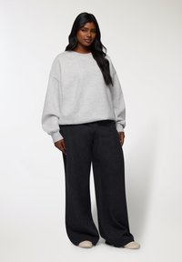 Felpa in pile grigia chiara con spalle cadenti, abbinata a pantaloni neri larghi. L'outfit presenta un design a gamba larga e una texture morbida.