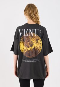 T-shirt oversize nera con un grande grafico di un pianeta giallo e testo sul retro, maniche corte e vestibilità comoda.