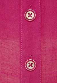 Details van een roze stoffen shirt met twee ronde, zilveren knoppen met vier gaatjes, zichtbare stiksels en een textuur van lichte stof.