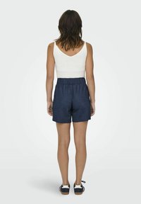 Débardeur blanc à fines côtes associé à un short à cordon de serrage bleu marine. Tissu doux, coupe décontractée et longueur mi-cuisse. Des chaussures décontractées complètent le look.