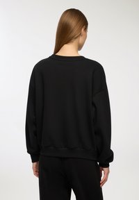Felpa nera oversize con scollo rotondo, spalle abbassate, polsini e orlo a costine. Texture liscia, design casual e vestibilità rilassata.