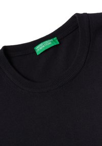 Černý svetr s vroubkovaným výstřihem. Textura látky je hladká. Obsahuje zelenou nálepku s nápisem "UNITED COLORS OF BENETTON."