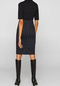 Mörkblå rutigt blyertskjol med en figurnära design, tillverkad av strukturerad tyg. Bärs med en svart kortärmad topp och knähöga svarta stövlar.