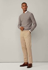 Harmaa, tekstuuroitu neulepaita pyöreällä pääntiellä, yhdistetty beigen värisiin housuihin. Malli pukeutunut ruskeisiin nahkakenkiin, kädet taskuissa.