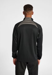 Pullover sportivo nero in tessuto testurizzato, colletto alto e dettagli grigi sulle spalle; presenta maniche lunghe e una vestibilità aderente.