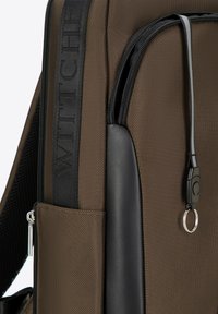 Zainetto marrone con tessuto texturizzato, dettagli neri lucidi e una tracolla verticale con il logo "WITTHI". Include una tasca con zip e un portachiavi.