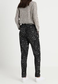 Zwarte joggers met patroon, elastische tailleband, zijzakken en tapered benen. Gecombineerd met een grijze gebreide trui en witte sneakers.