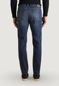 Jean en denim bleu foncé avec une coupe droite, doté d'un patch en cuir au dos de la taille et de deux poches arrière ; détails de couture visibles.