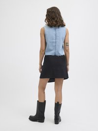 Denim ermeløs topp med et kort design, kombinert med et svart skjørt. Modellen har på seg kne-høye svarte skinnstøvler.