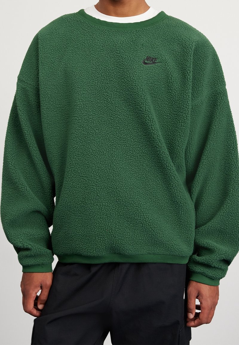 Zelená fleecová mikina s texturovaným povrchem, žebrovanými manžetami a límcem. Obsahuje malé černé logo Nike na hrudi.