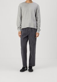 Grijze lange mouwen shirt met een gemarmerd patroon, gecombineerd met donkergrijze corduroy broek. Model draagt zwarte sneakers met witte accenten.