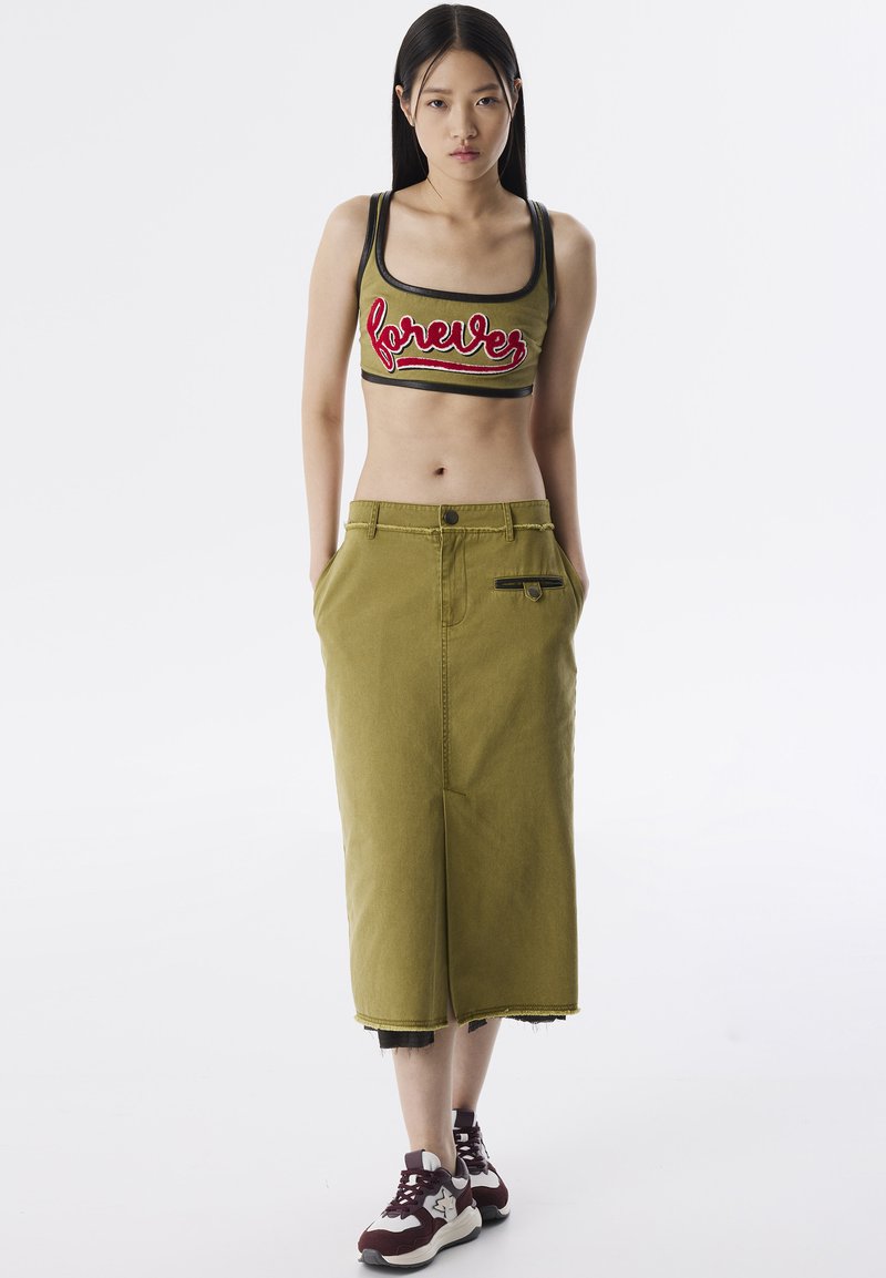 Jupe en denim vert olive avec fente avant et poches latérales, associée à un crop top ajusté vert olive ornée d'une broderie rouge.