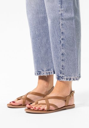 Sandales en cuir marron avec des brides croisées, une semelle plate et un détail de boucle à la cheville, assorties à un jean droit délavé.