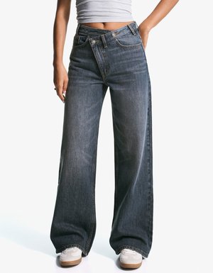 Weite Jeans aus Denim in Dunkelblau. Hochgeschnittenes Design mit glatter Textur und sichtbaren Nähten. Tragen mit weißen Sneakern.