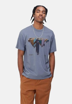 Camiseta gris de mangas cortas con un diseño gráfico multicolor que presenta la palabra "carhartt". La tela parece ligera. Lleva puestos pantalones marrones.