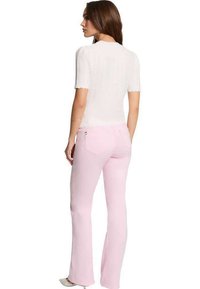 Jeans a campana rosa chiaro con tasche posteriori, abbinati a una maglietta bianca a maniche corte con texture e bordi scallop.