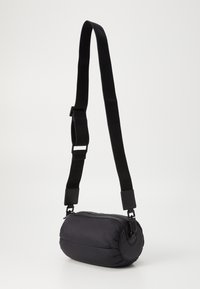 Borsa a tracolla nera a forma cilindrica con una texture imbottita, tracolla regolabile e chiusura con zip. Il materiale sembra essere nylon o poliestere morbido.