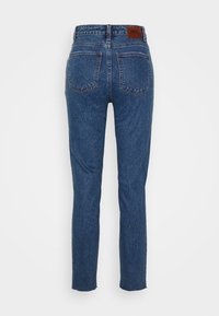 Jeans de denim azul con un diseño de pierna recta, cinco bolsillos y un parche trasero de cuero marrón. La tela tiene una ligera textura.