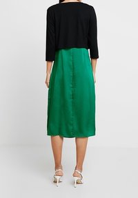 Mustaväri cropped-top yhdistetty vihreään satiiniseen midi-mekkoon, jossa on sileä pinta ja sivuaukko, täydentää valkoiset korot sandaalit.