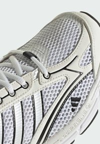 Witte sportschoen met een bovenwerk van mesh, synthetische overlays, zwarte accenten en een vetersysteem. Voorzien van een gedempte zool en een geprofileerd oppervlak.