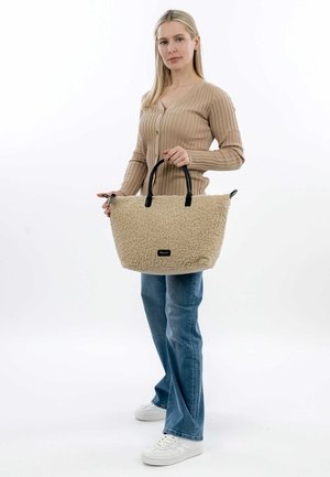 Beige shearling tote bag with black handles, featuring a rectangular shape and textured surface. Secure zipper closure on top.
