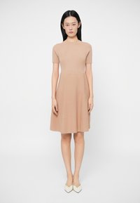 Vestido de malha de manga curta em bege claro, com corpete ajustado e saia ampla. Textura suave, padrão amarelo listrado discreto, até ao joelho.