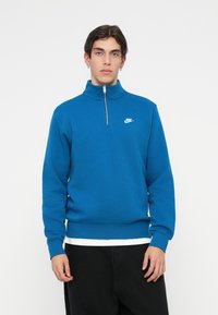 Μπλε φούτερ με φερμουάρ στο λαιμό φτιαγμένο από μαλακό υλικό, με λευκό λογότυπο Nike στο στήθος και ριμπ μανσέτες και στρίφωμα.