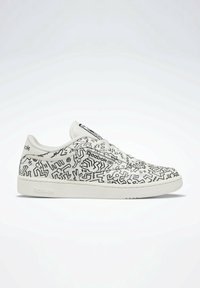 Baskets blanches avec motifs abstraits noirs, dotées d'un design profil bas, fermeture à lacets et semelle en caoutchouc texturée. Logo Reebok visible.