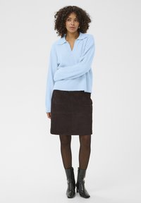Pull tricoté bleu clair avec un col, associé à une jupe en daim brun foncé avec deux poches avant, et des bottines noires à talons.