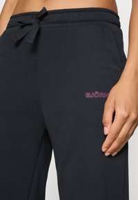 Čierne tepláky s vlastnosťou sťahovacej šnúrky v páse, s malým ružovým logom "BJÖRN" na boku, vyrobené z mäkkej, texturovanej tkaniny.